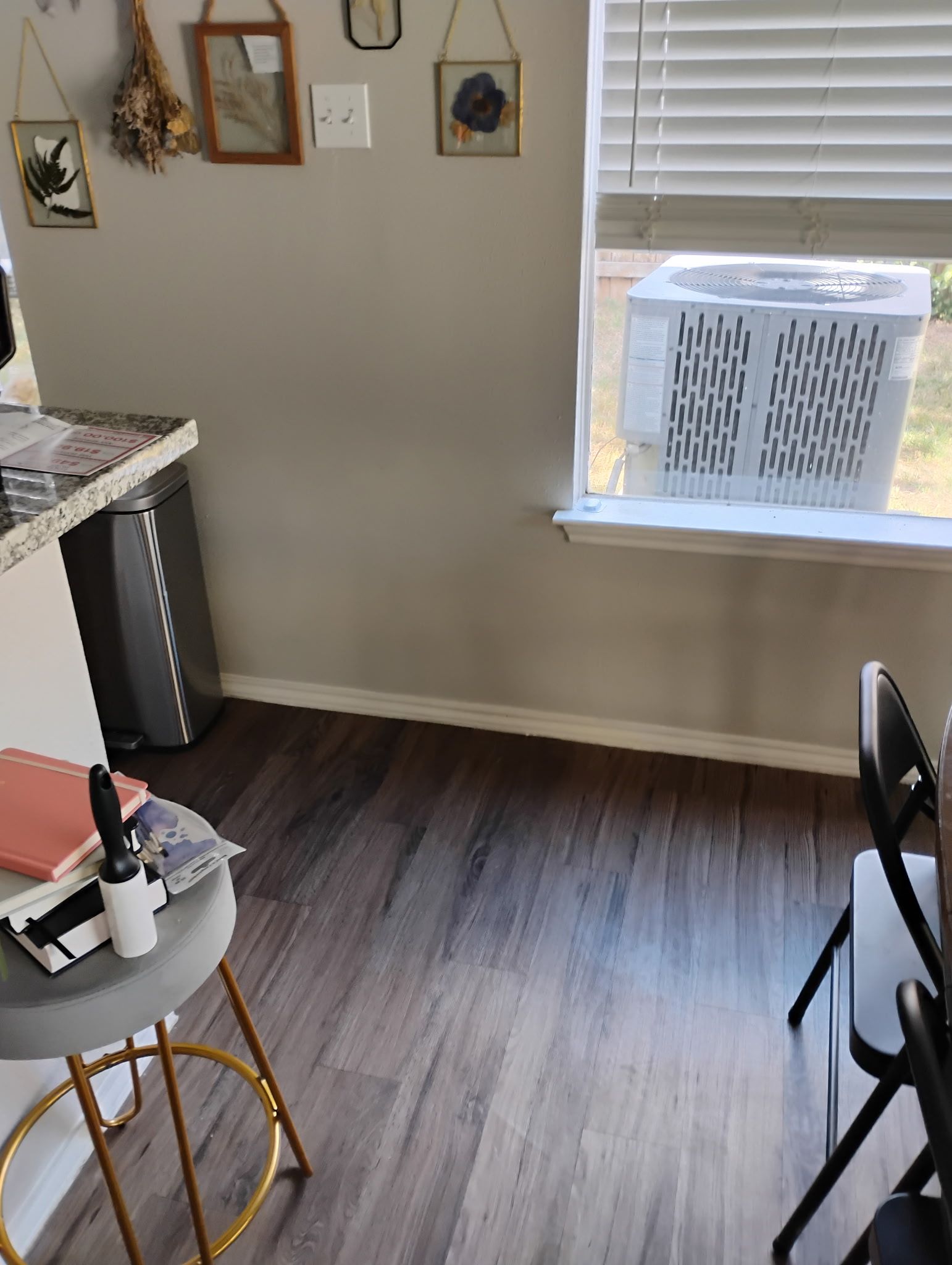 Room with air conditioner in window, stool, dark wood floor, and decorative wall hangings.