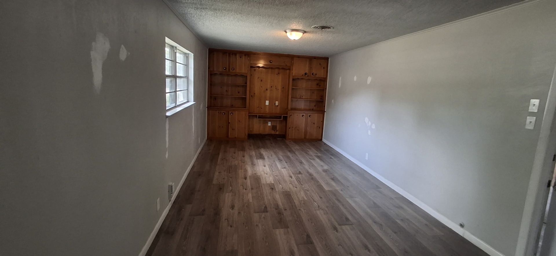 Empty room with built-in wooden cabinets. Grey walls, light-colored floor, a small window.
