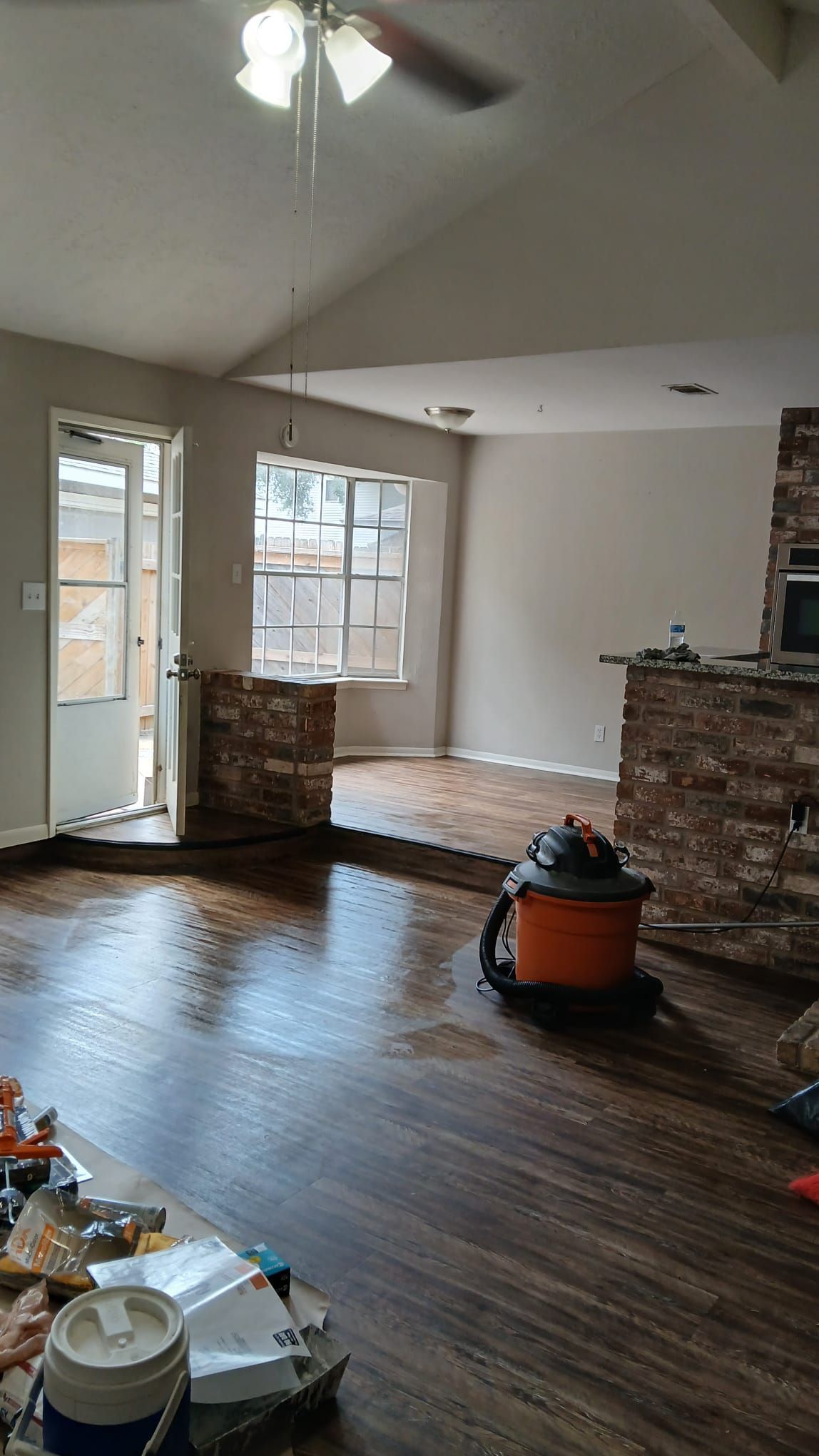 Interior renovation, living room with wet flooring and exposed brick. Vacuum cleaner sits on the floor.