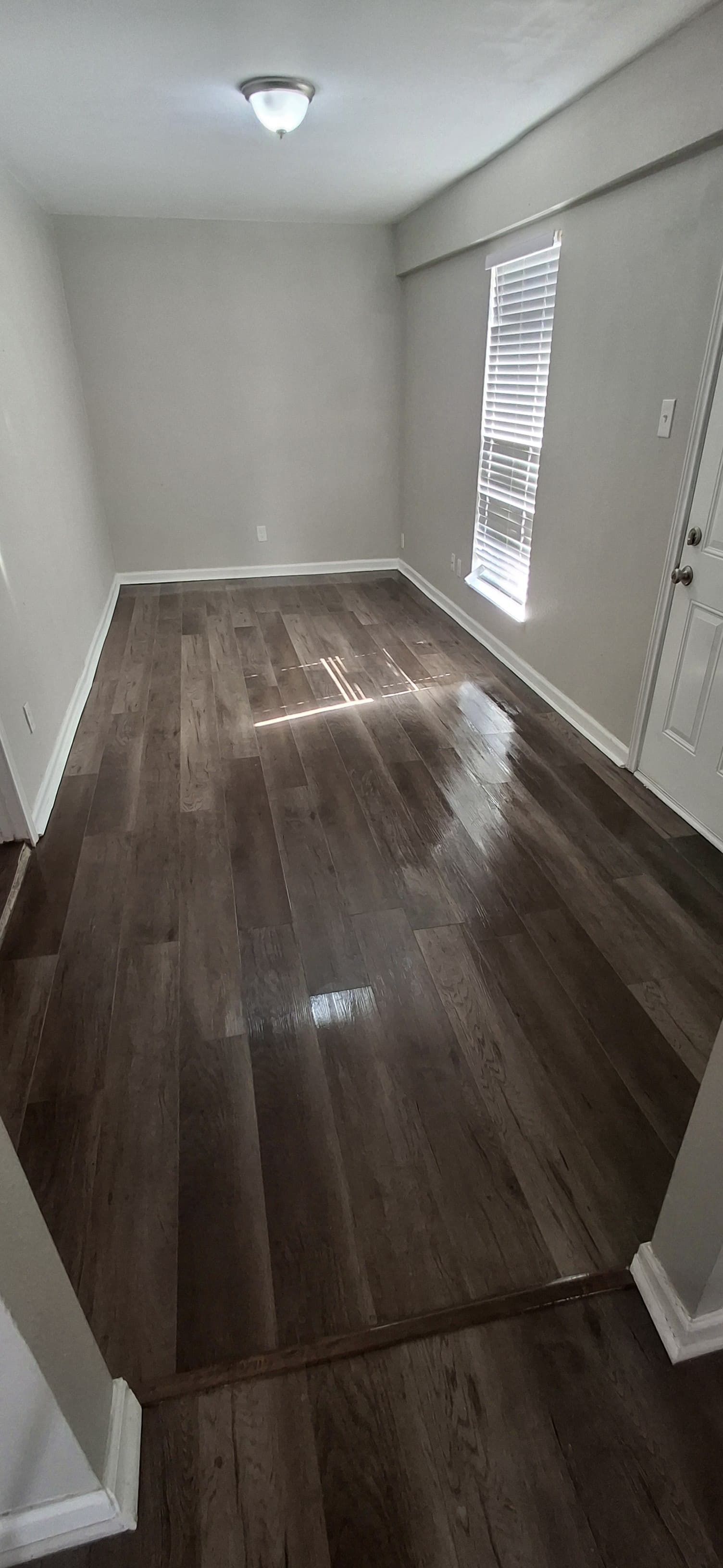 A small room with wood flooring, light-colored walls, and a window with blinds.