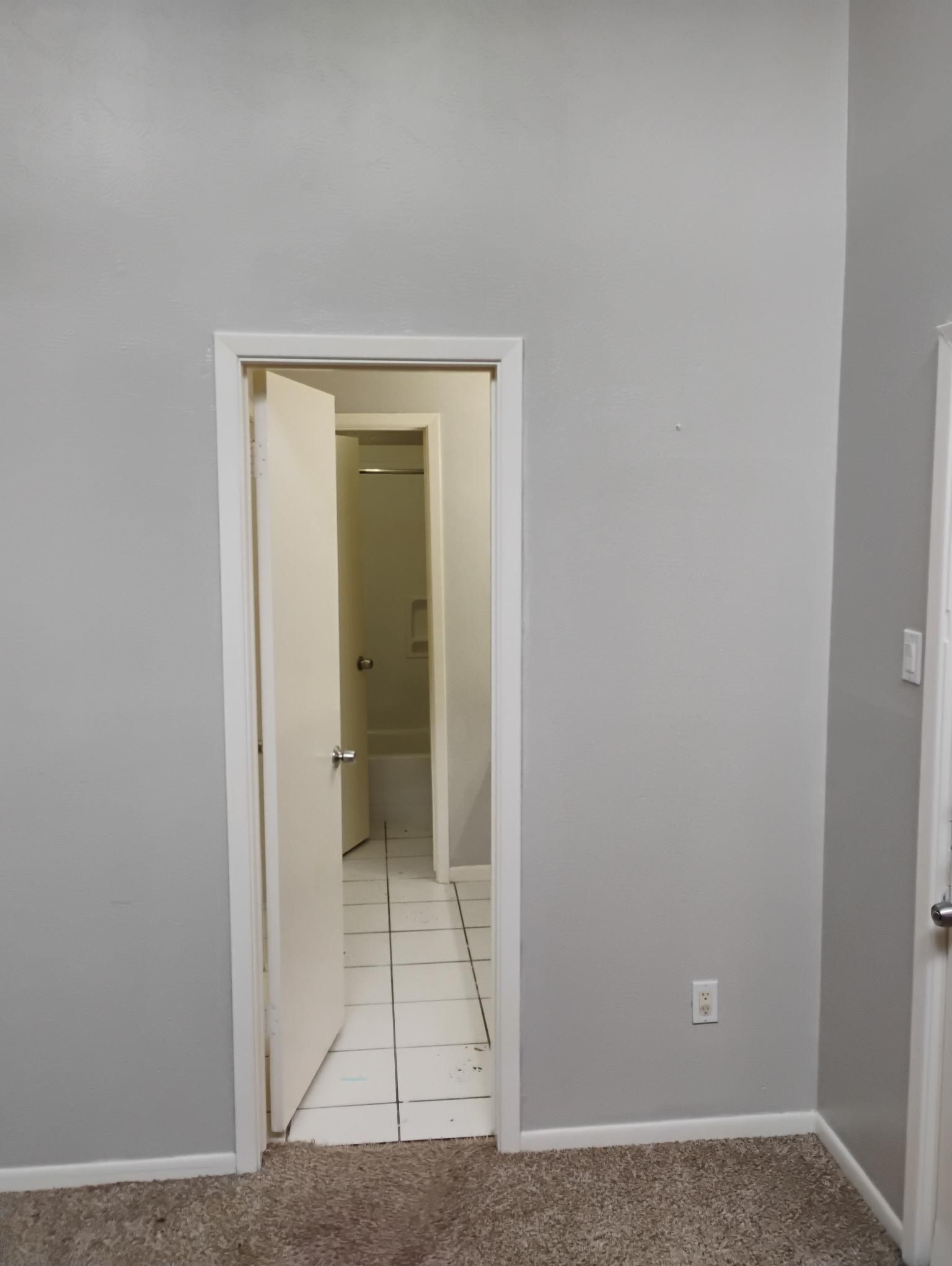 A doorway with a partially open door reveals a bathroom with a bathtub, white tile floor, and gray walls.