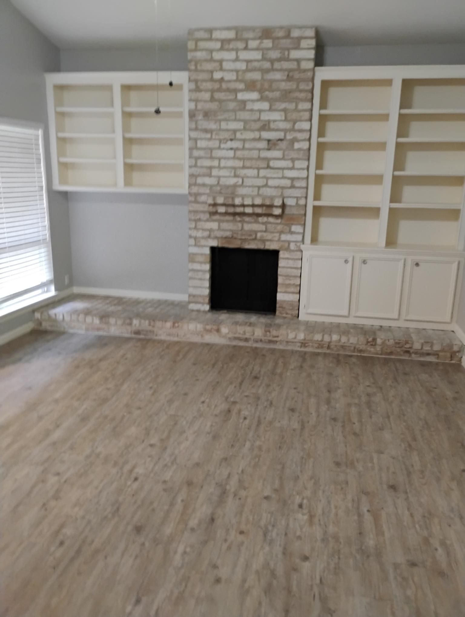 Living room with brick fireplace, built-in shelves, and wood-look flooring.