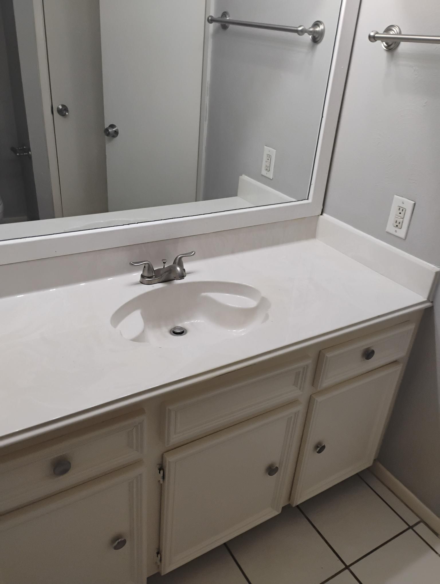 White bathroom vanity with sink and mirror, silver fixtures, and white countertop against gray walls.