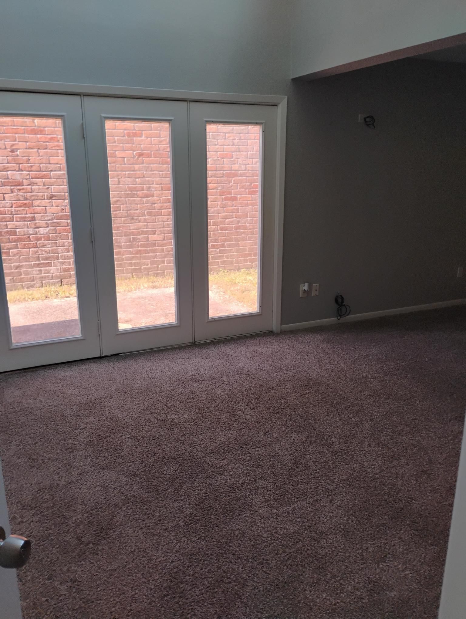 Room with new brown carpet, white French doors, and a brick exterior. Gray walls.