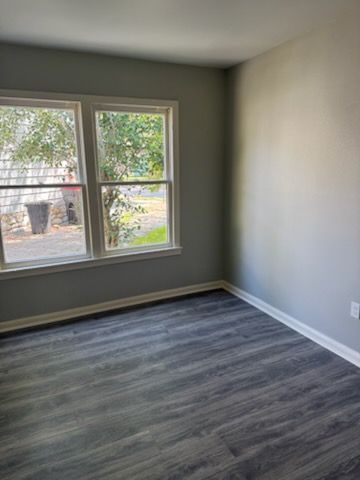 Empty room with gray walls, dark wood-look floor, and two-paned window looking outside.