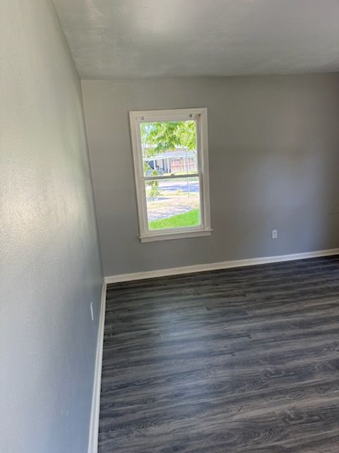 Empty room with gray walls, a window, and dark wood-look flooring.