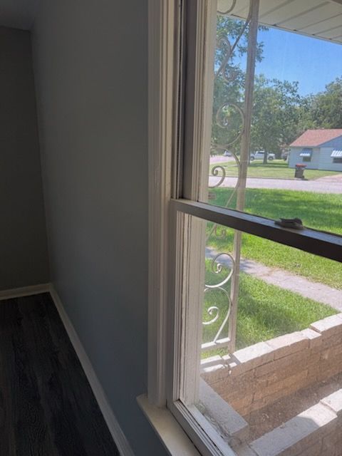 Interior view of a window with decorative metal bars, looking out to a residential street with green grass and a house.