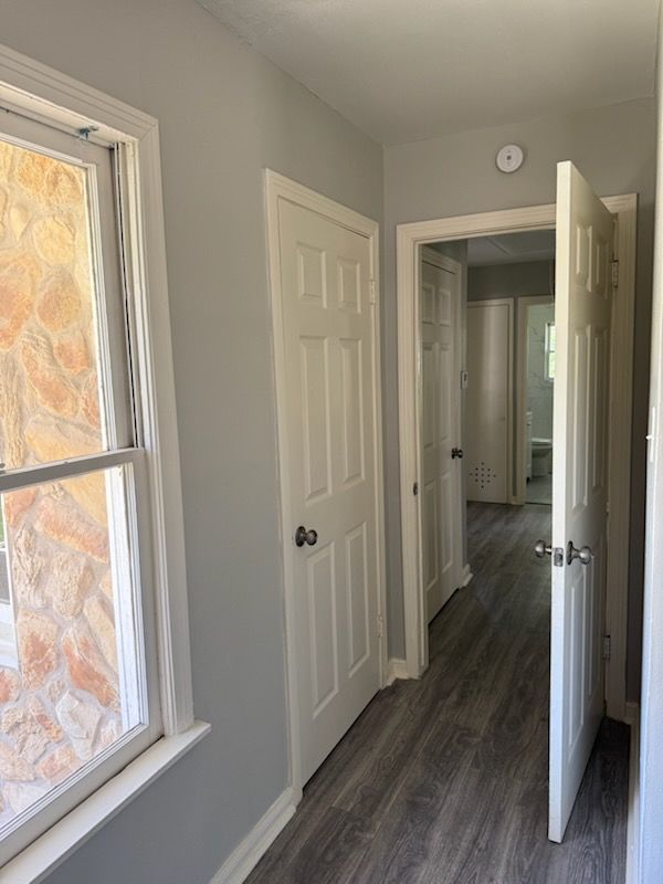 Narrow hallway with gray walls, white doors, and a window with stone detail.