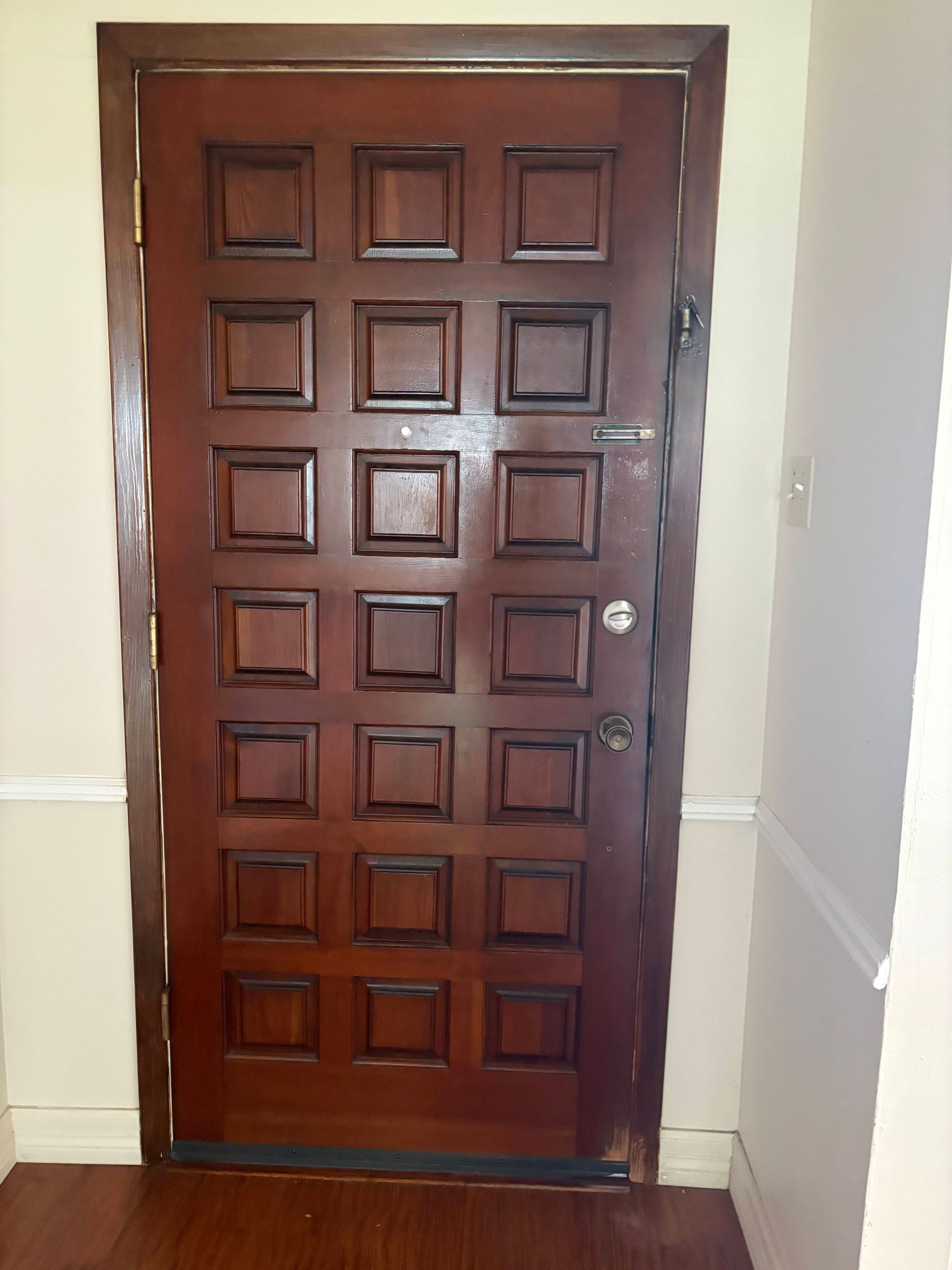 Wooden door with square panels, in a hallway with light-colored walls and floor.