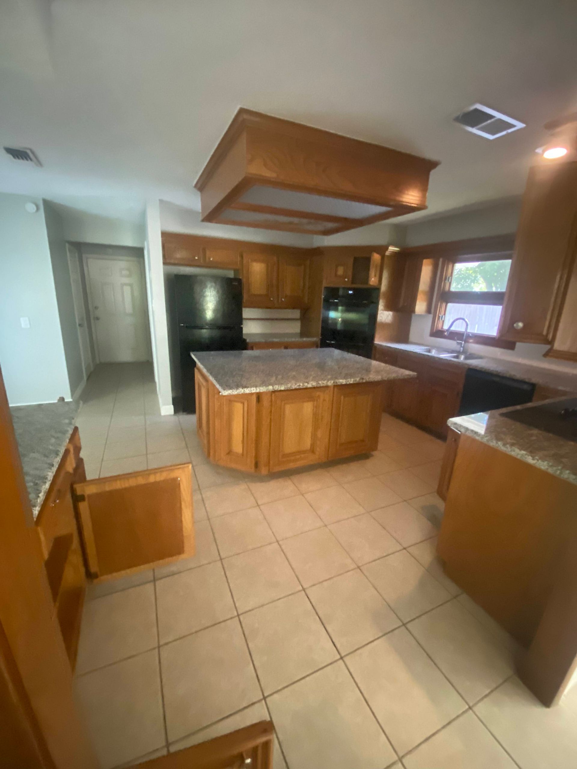 A kitchen with wooden cabinets and island, granite countertops, tile floors, and a black refrigerator.