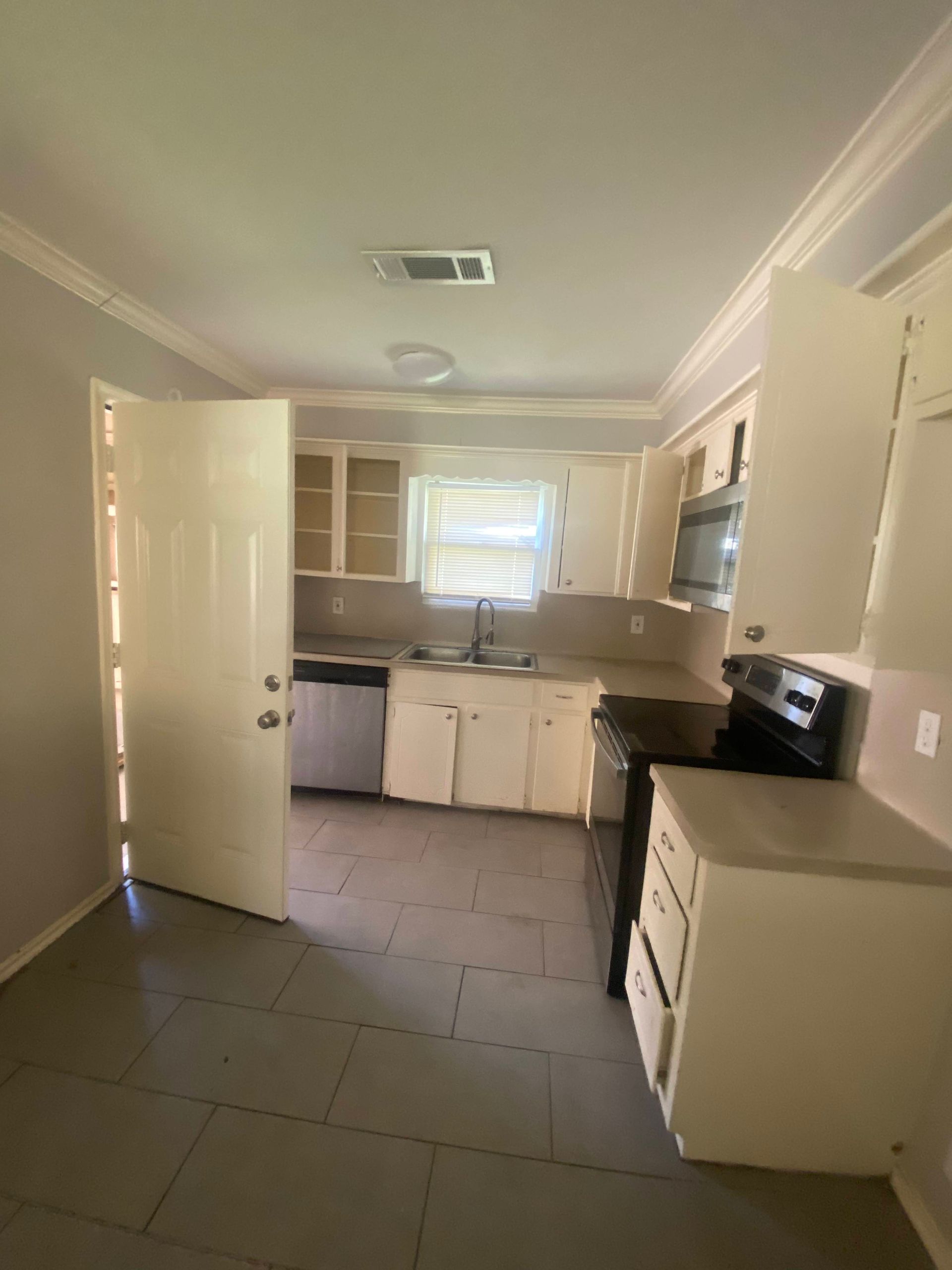 A kitchen with white cabinets, appliances, and a gray tile floor. A door is ajar on the left.