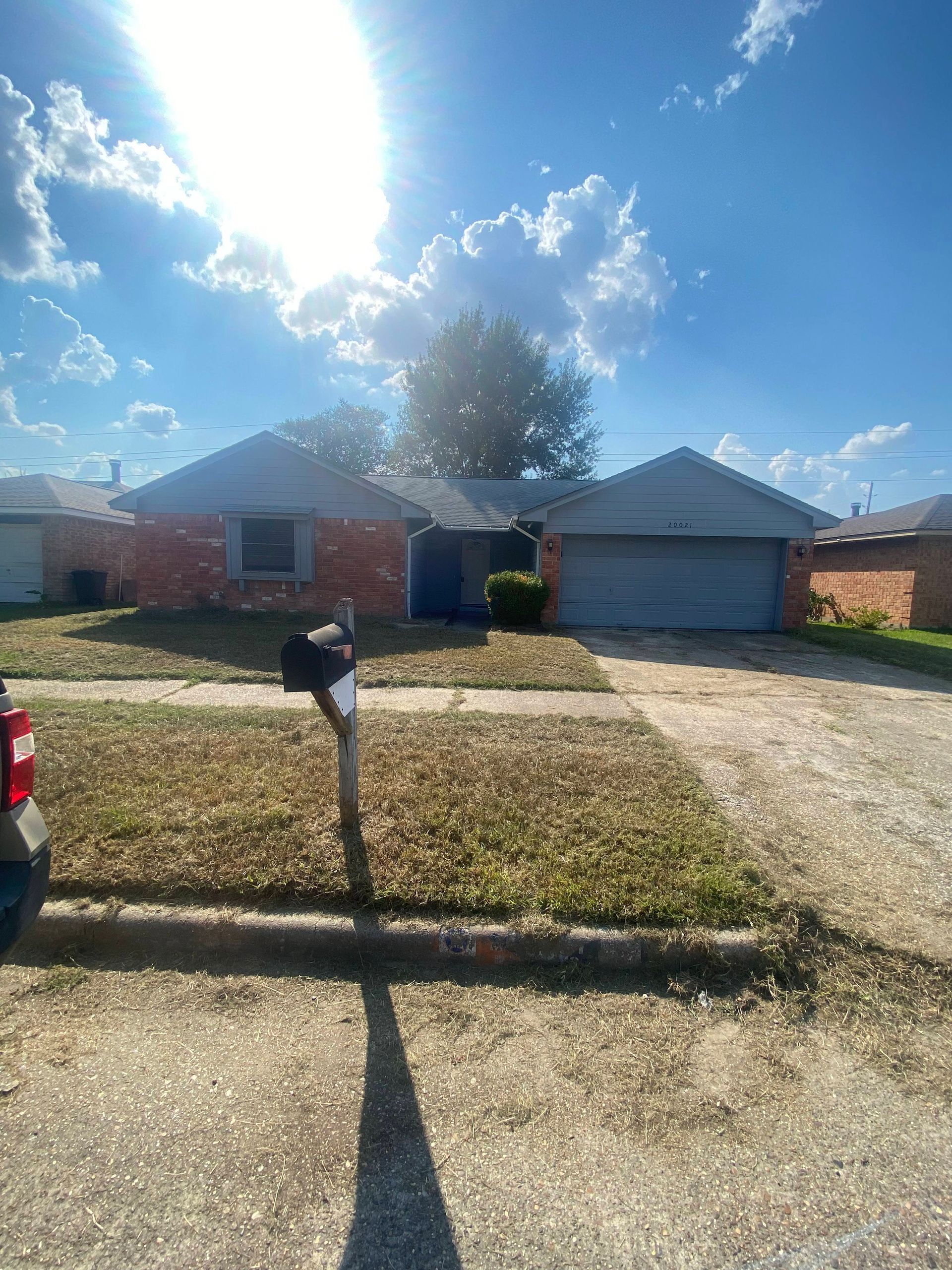 Suburban single-story brick house with a mailbox in front, blue sky, and a sunny day.