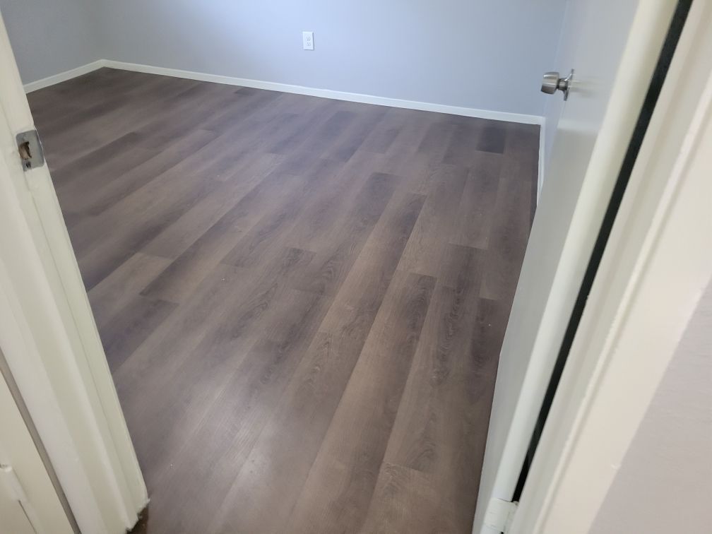 Empty room with gray wood-look flooring and white trim. Doorway on the right.