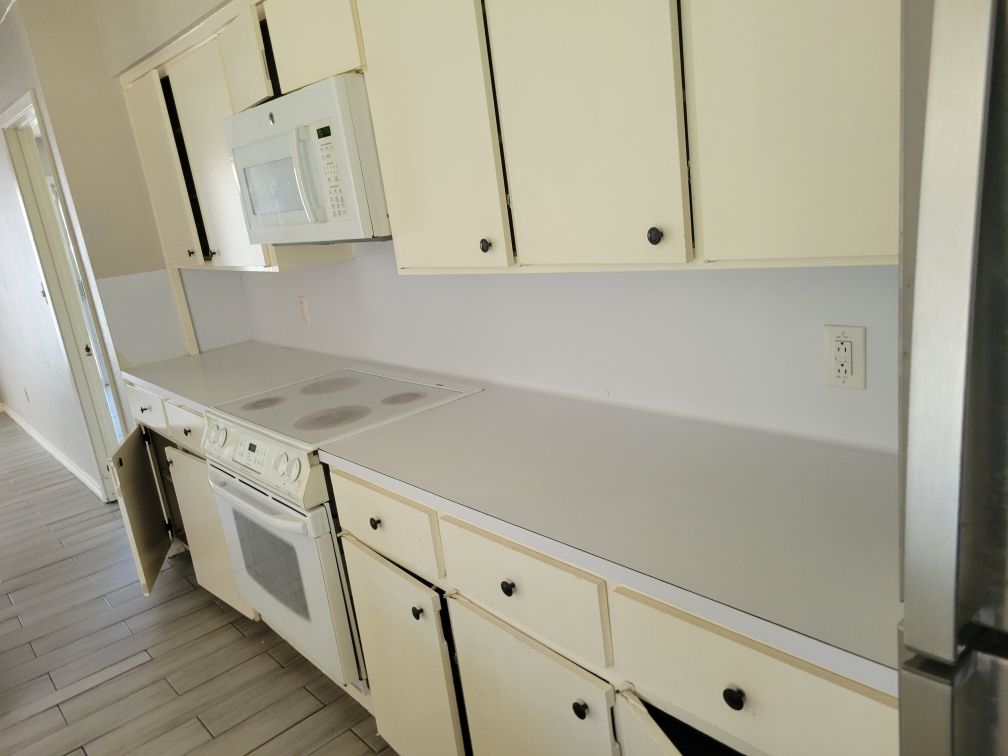 White kitchen cabinets and appliances with a countertop. The oven door is open.