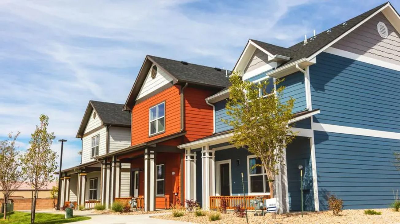 Row of colorful two-story townhouses with dark roofs. Blue sky with clouds overhead.