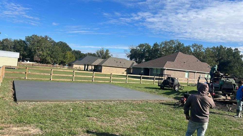 Concrete slab, fence, houses, workers, and trees on a sunny day.
