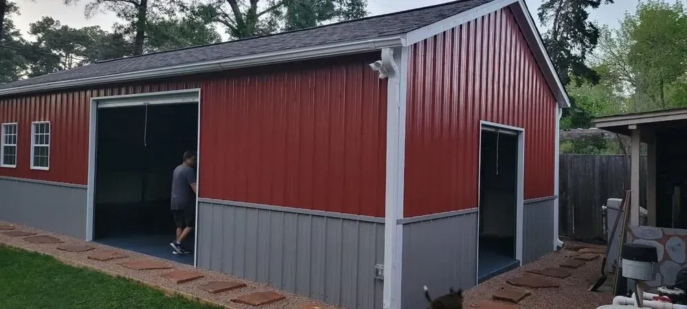 Red and gray metal building with open garage door; person inside.