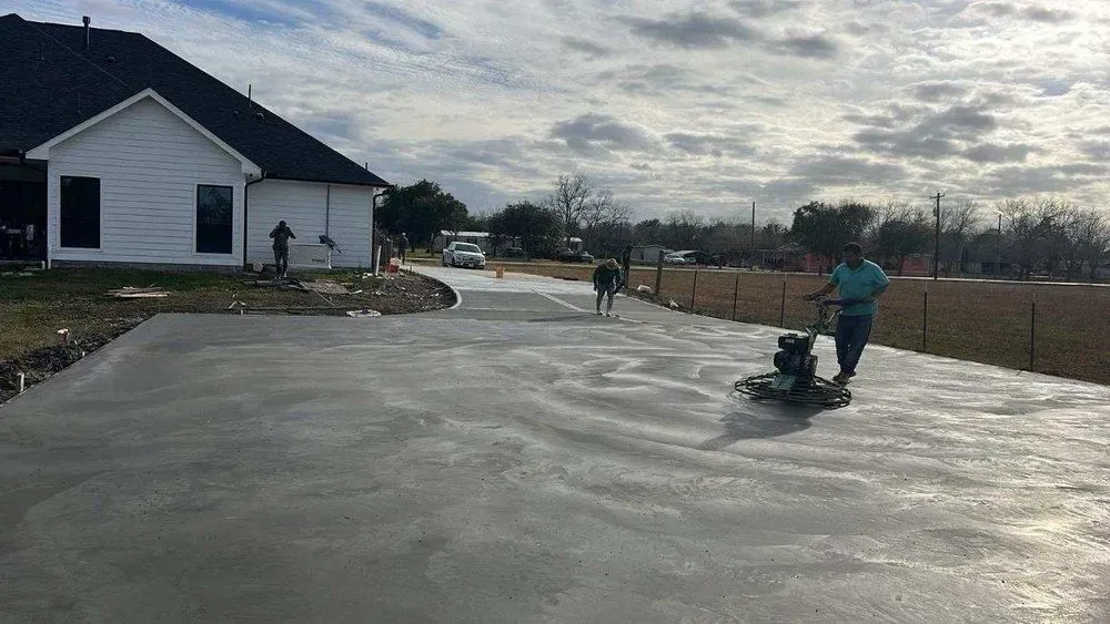 Man using concrete grinder on driveway in front of a white house.