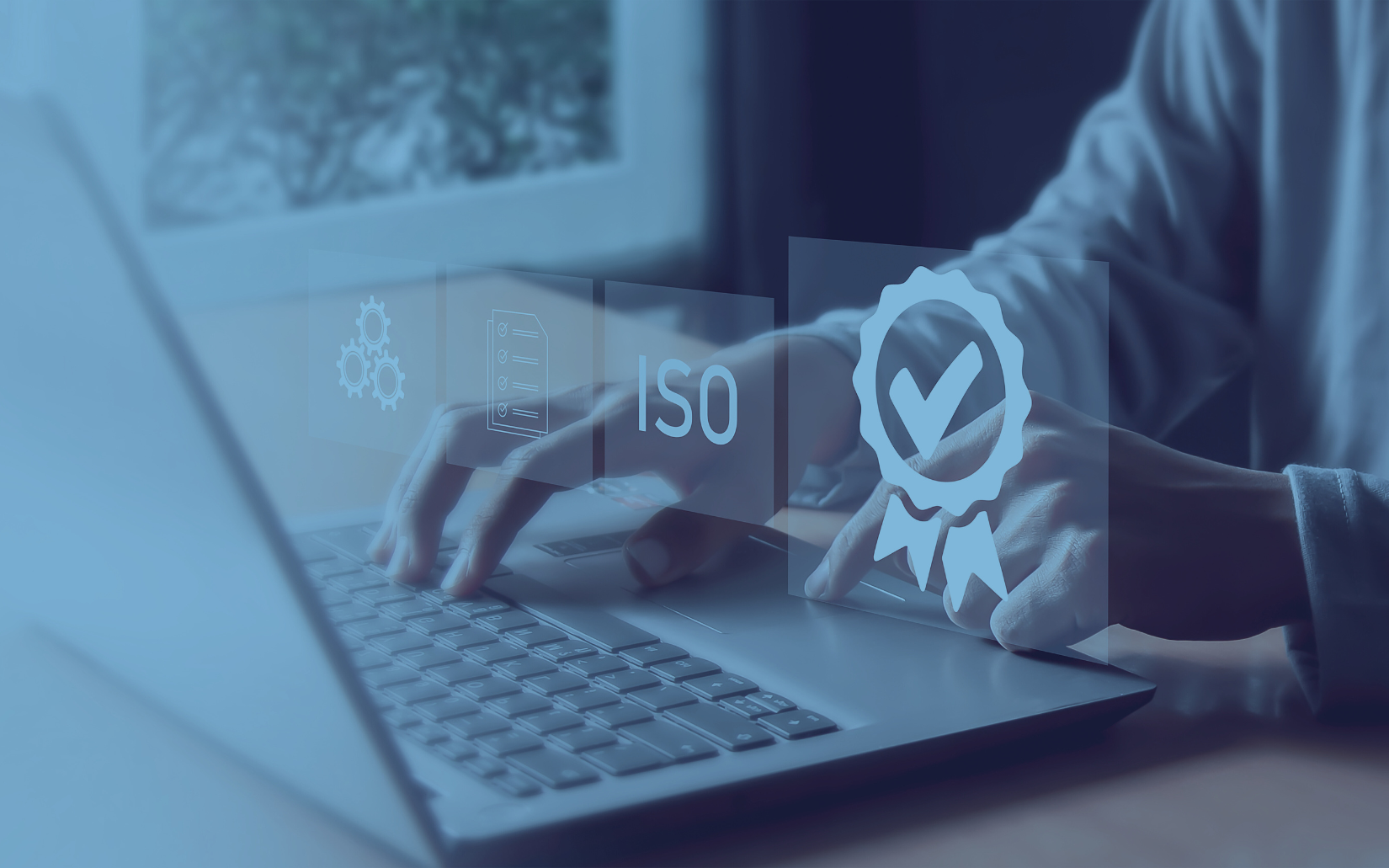 Person typing on a laptop, with an overlaid graphic of an ISO certification badge and related icons in shades of blue.