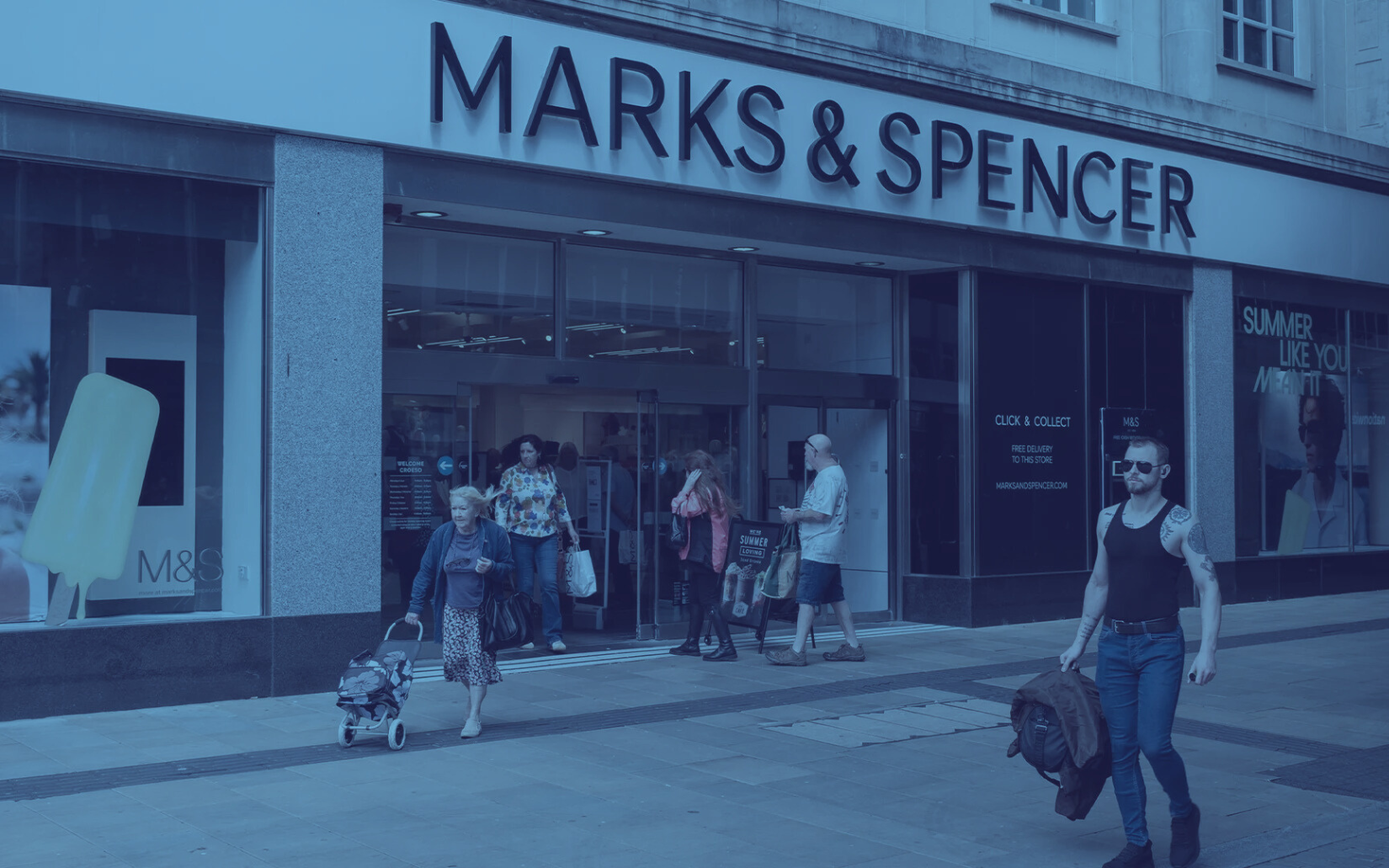 Exterior of Marks & Spencer store with several people entering and exiting. Signage above entrance.