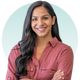 Smiling woman with dark hair and arms crossed, wearing a red shirt against a light blue backdrop.