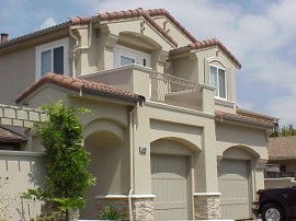 Beige two-story house with arched garage doors, a small balcony, and a red tile roof.