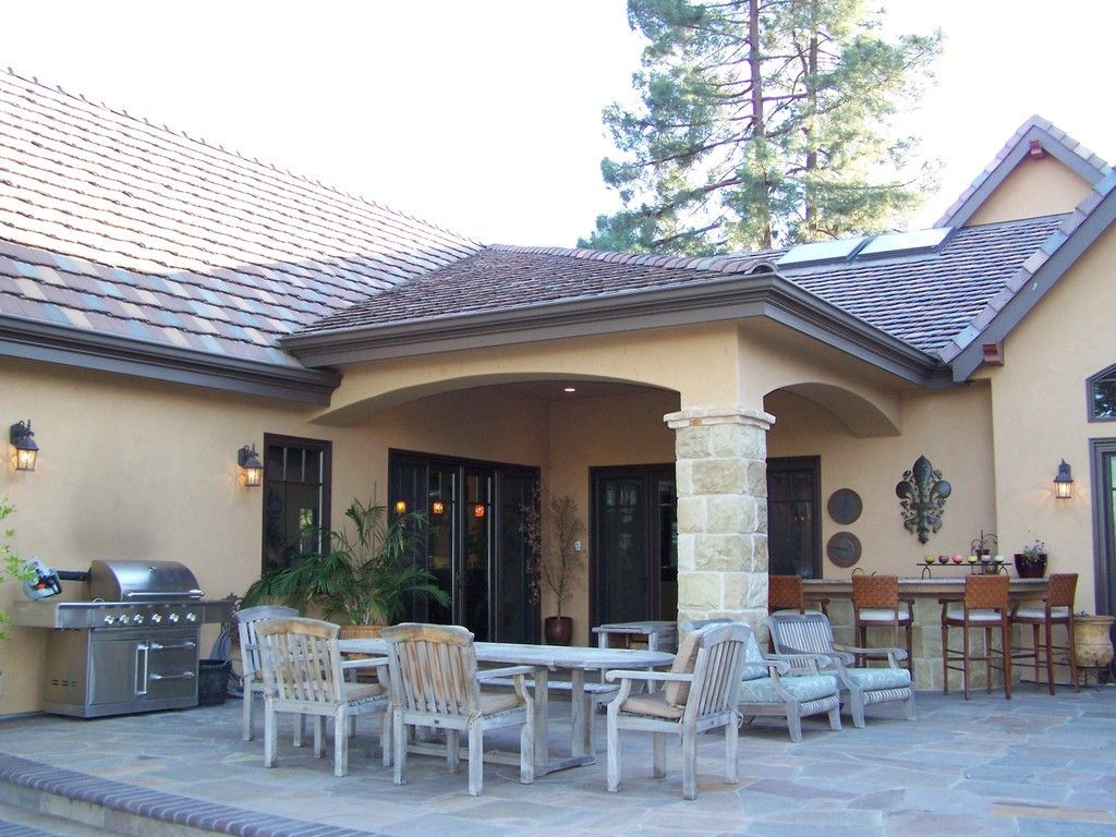 Patio with dining table, chairs, grill, and outdoor bar under a covered area, neutral colors.