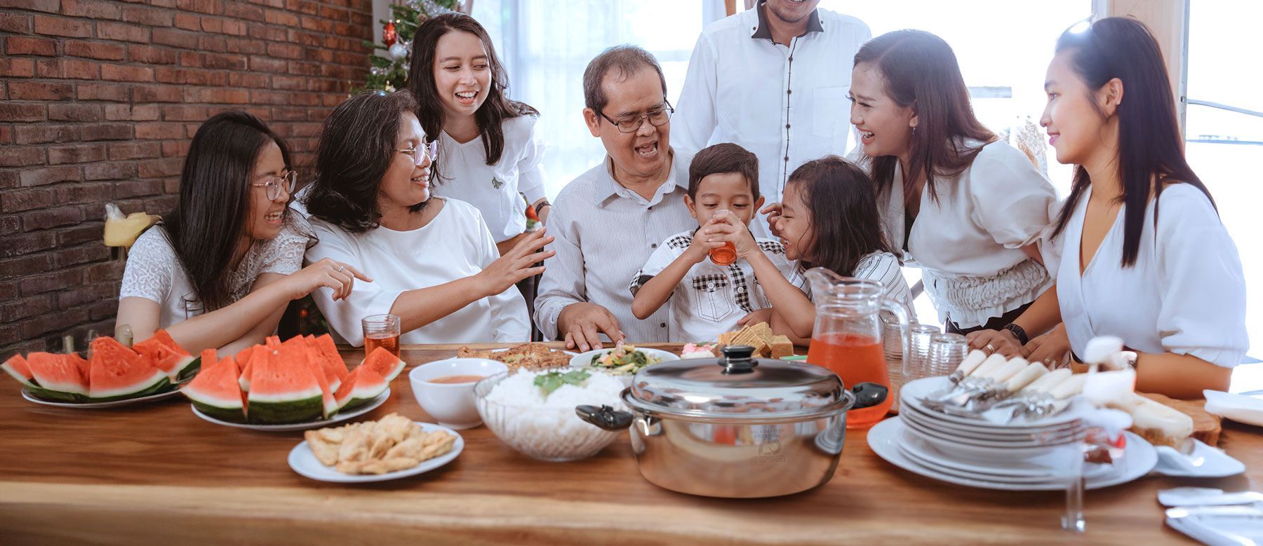 Family sharing a meal around a table with watermelon, dishes, and drinks in a cozy home setting