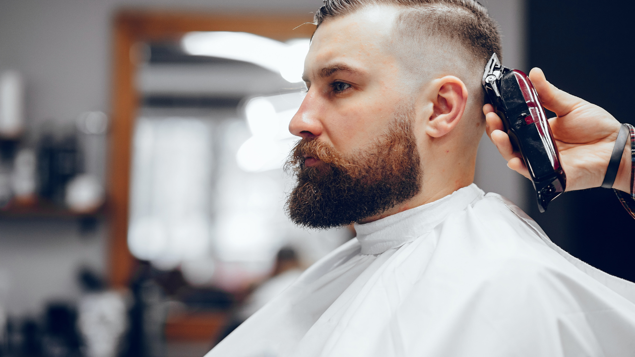 Man getting a haircut at a barbershop; barber using clippers to trim the sides.