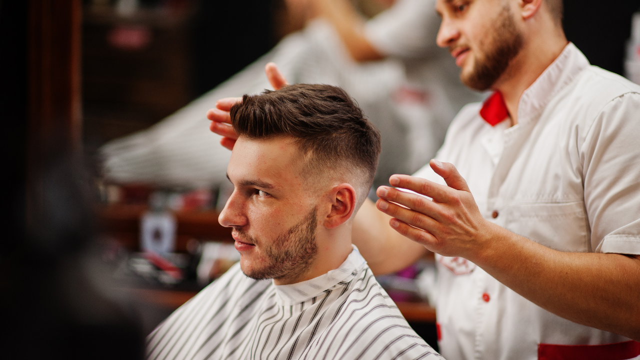 Man getting a haircut at a barbershop; barber styling hair.