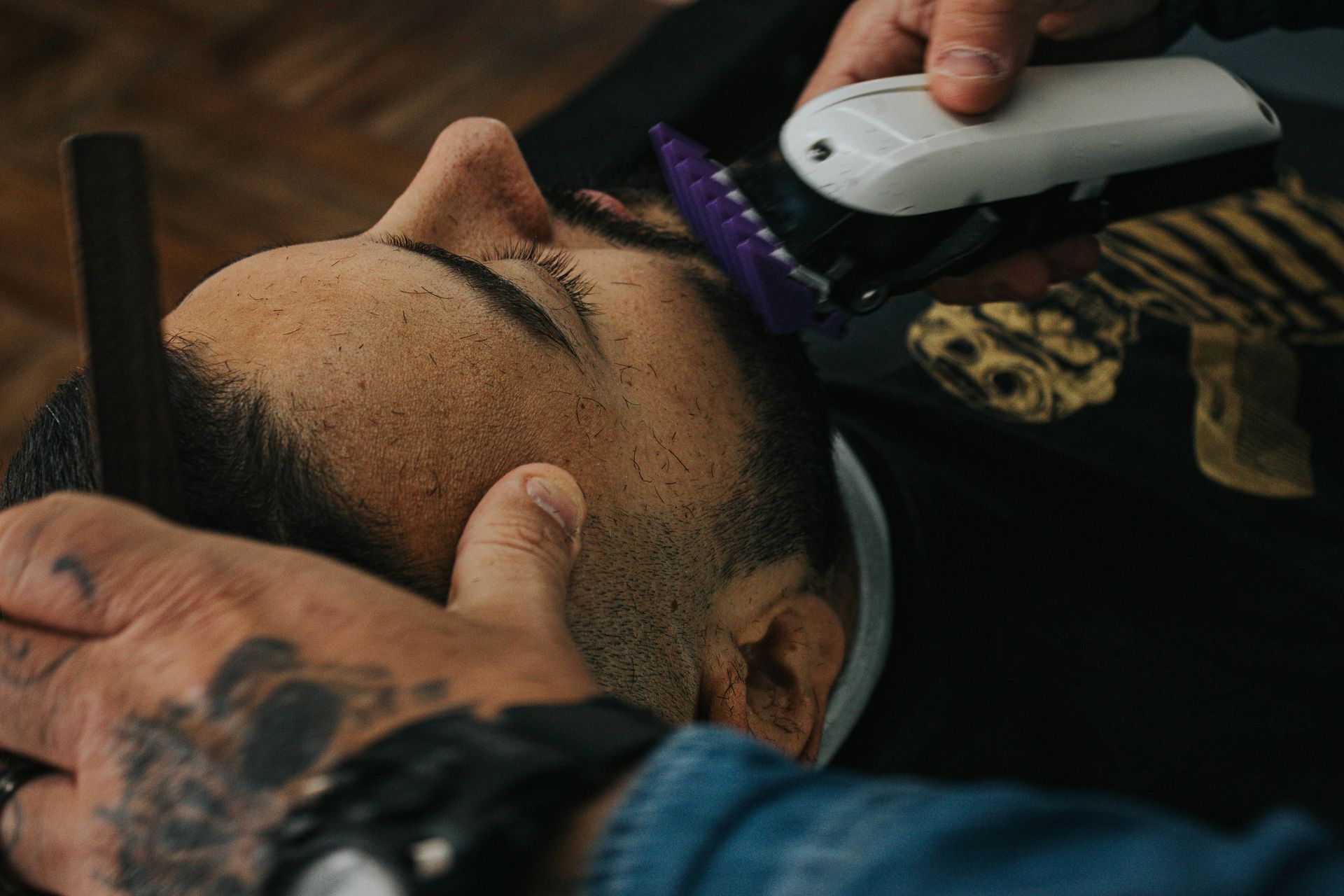 Barber trimming a person's facial hair with clippers and a comb in a barber shop setting.