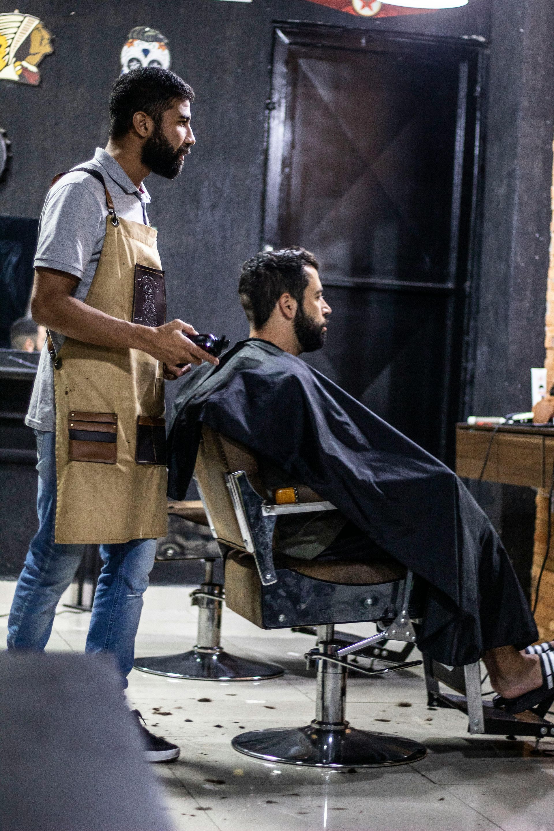 Barber using clippers to cut a customer's hair in a barbershop. The customer is seated in a chair.