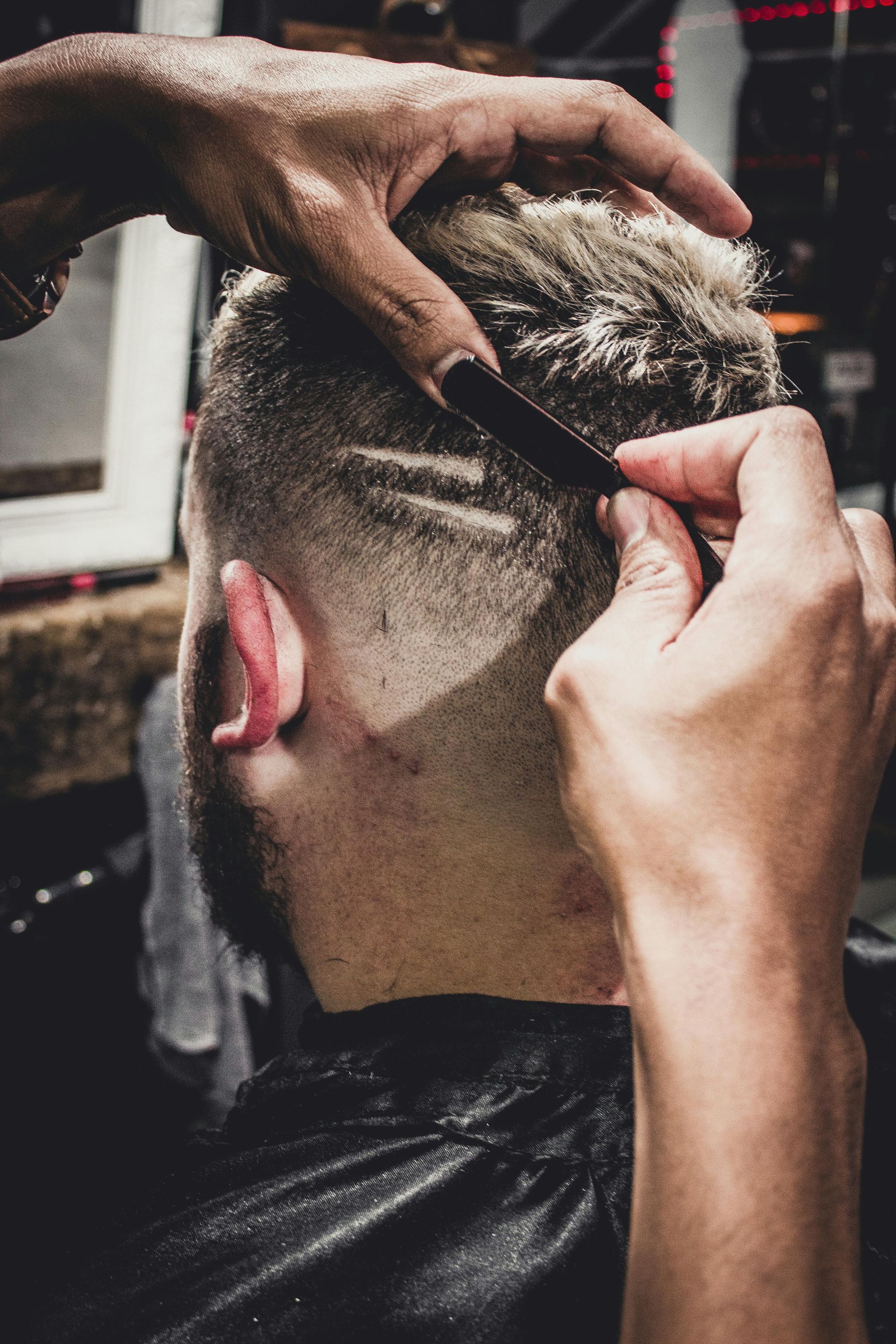 A barber cutting a client's hair with a straight razor in a barbershop.
