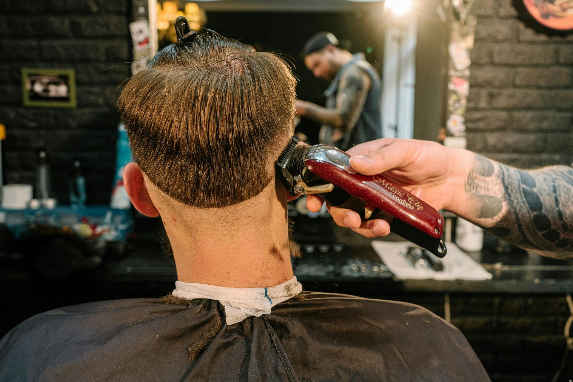 Barber trimming a client's neck with clippers in a salon, another barber in the background.