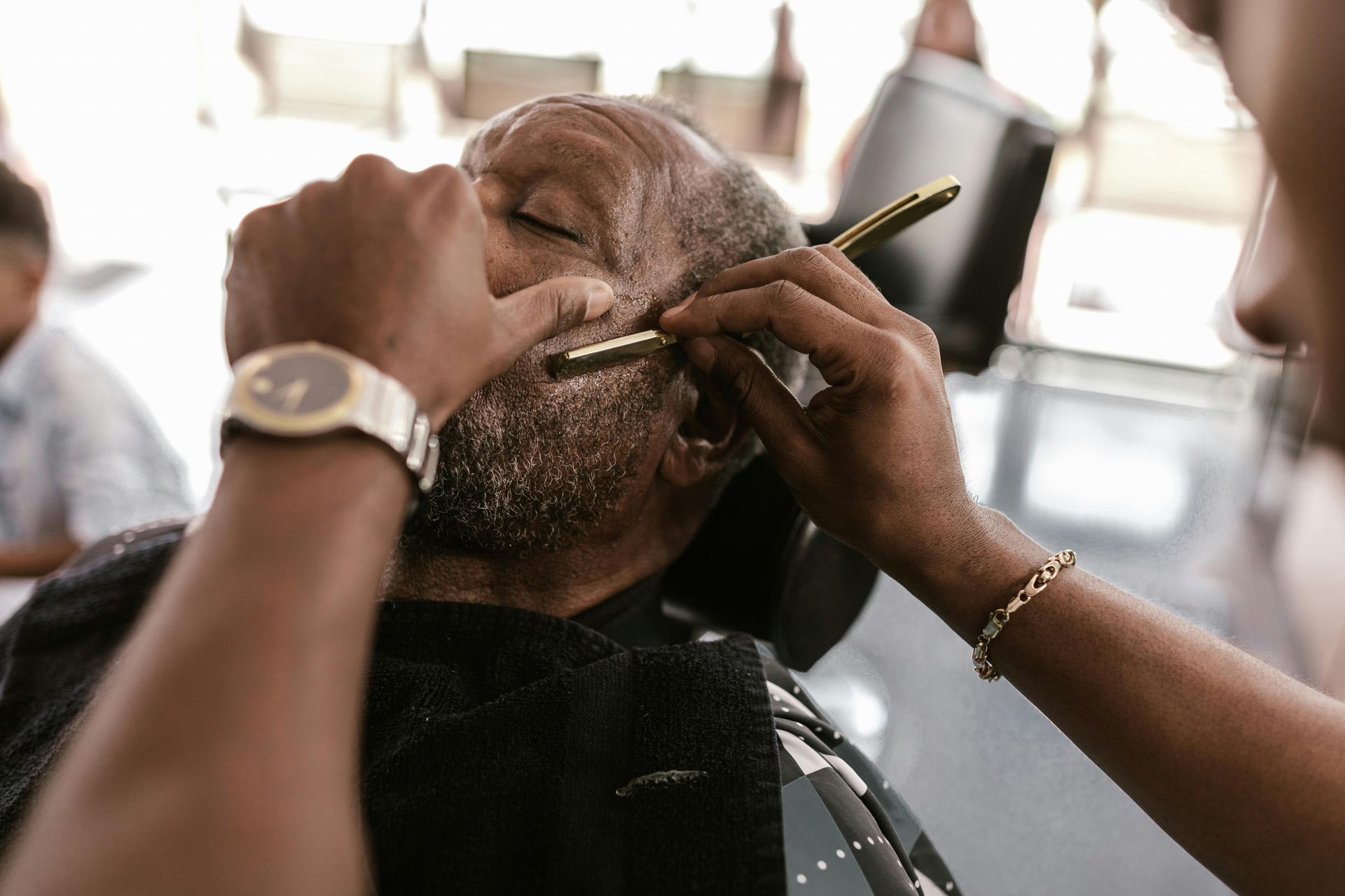 Barber shaves a person's face with a straight razor.