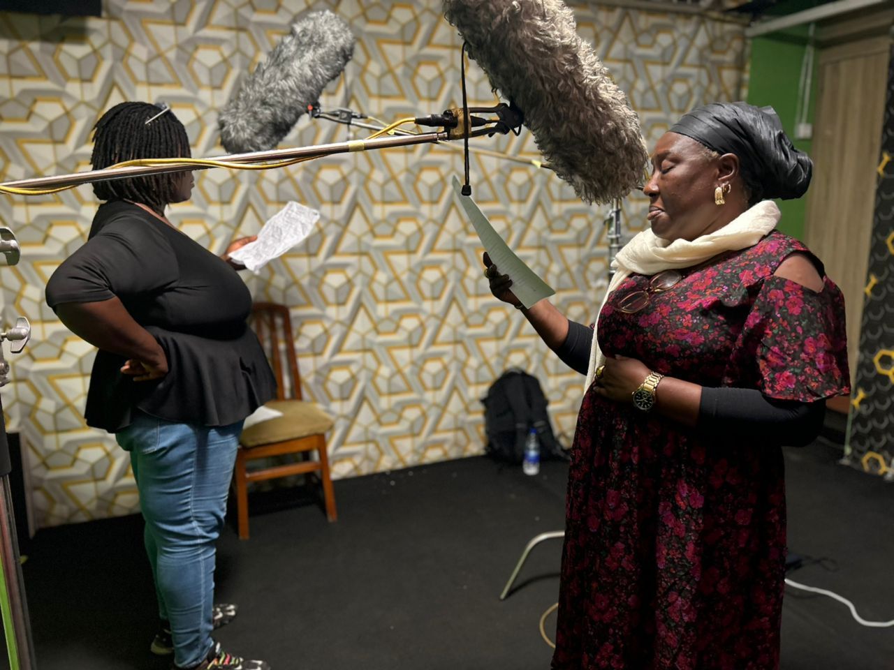 Two women in a recording studio; one holds a script, the other a boom mic.