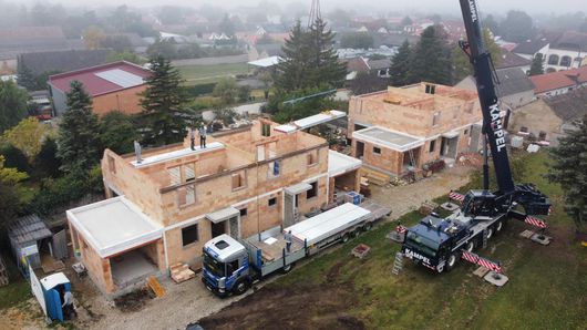 Zwei Bauarbeiter in Westen und Schutzhelmen besichtigen eine Baustelle, ein Kran ist zu sehen.