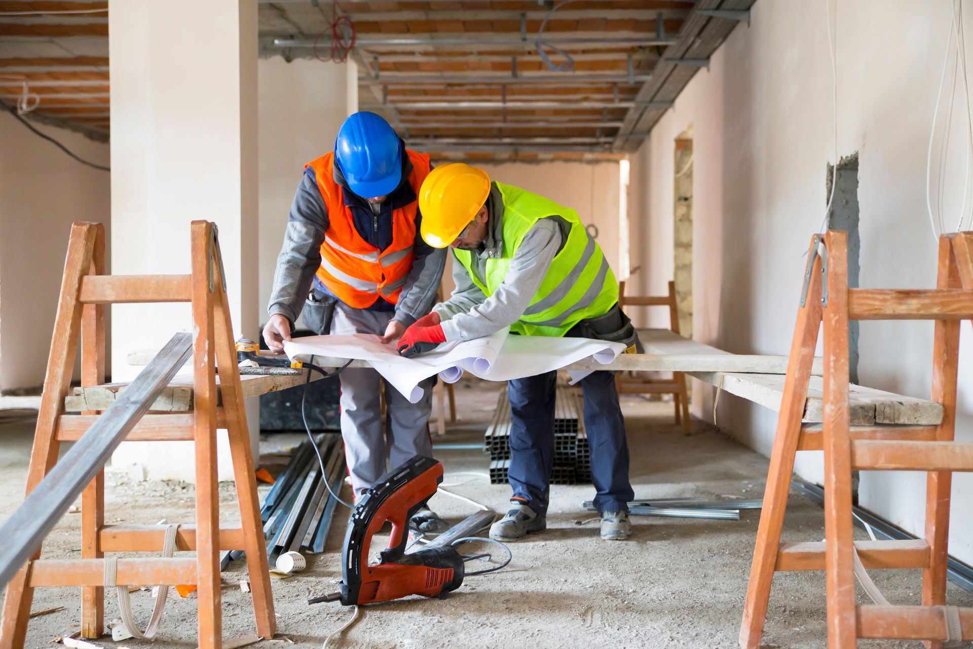 Zwei Bauarbeiter in Sicherheitswesten und Helmen prüfen Baupläne auf einer Baustelle.