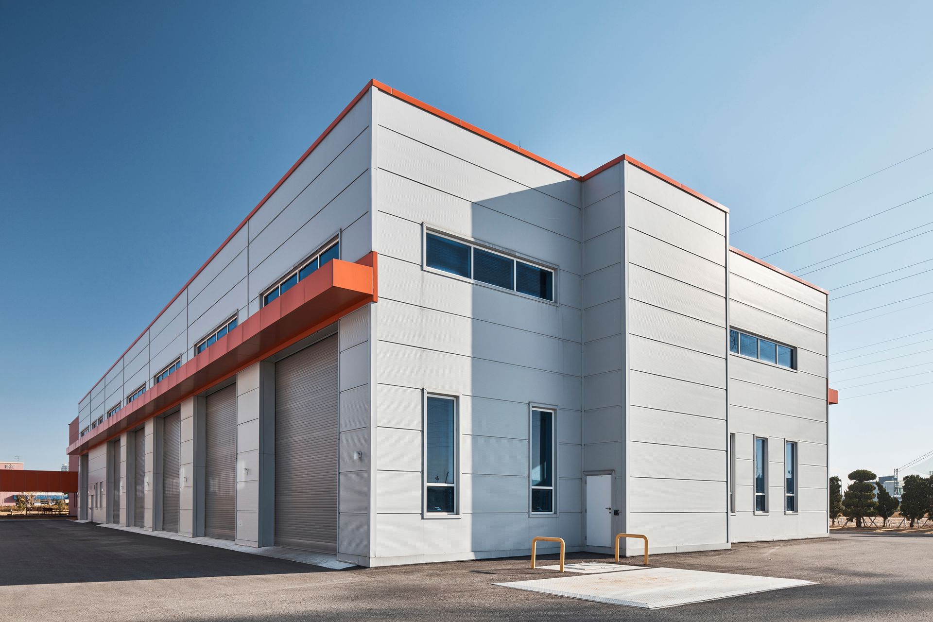 Graues Industriegebäude mit orangefarbenen Akzenten unter blauem Himmel; verfügt über Rolltore und Fenster.
