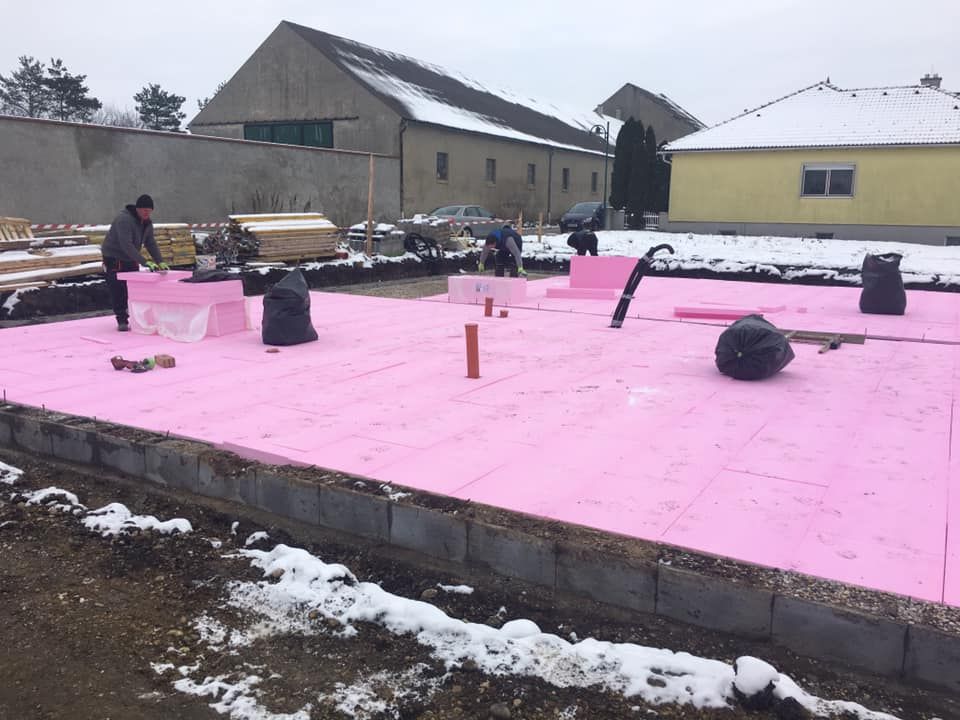 Baustelle mit rosa Dämmung, Arbeitern und verschneitem Hintergrund.