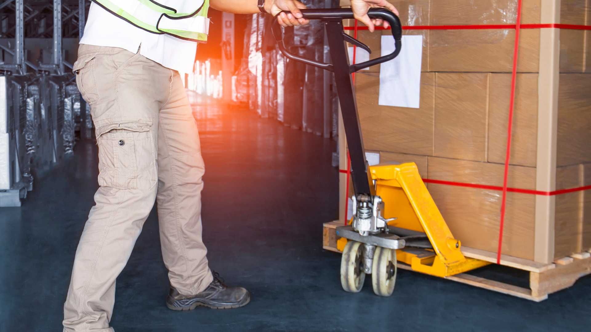 A man is pushing a pallet truck with boxes on it in a warehouse.