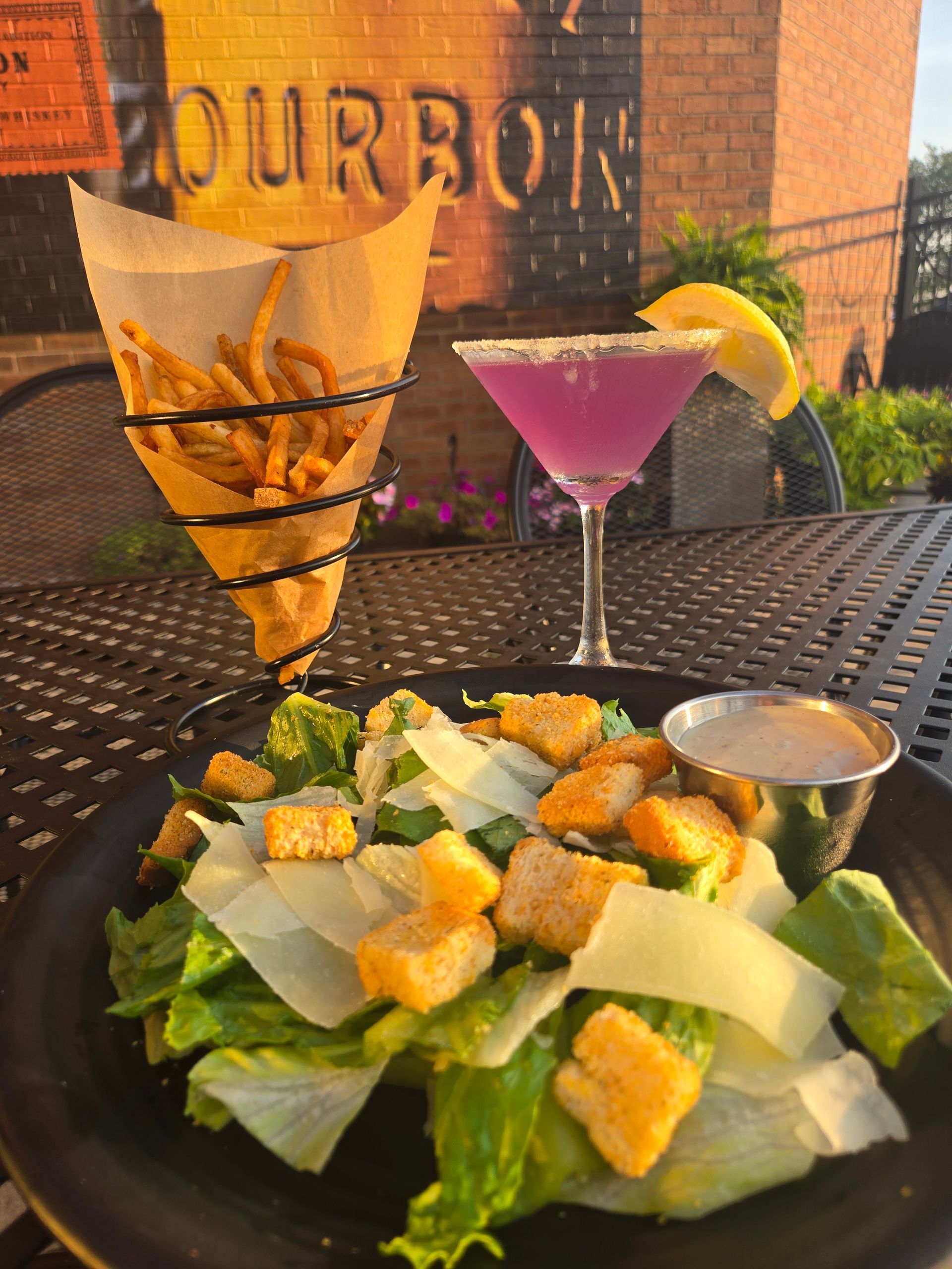 Salad with croutons and parmesan beside two cocktails on an outdoor patio table