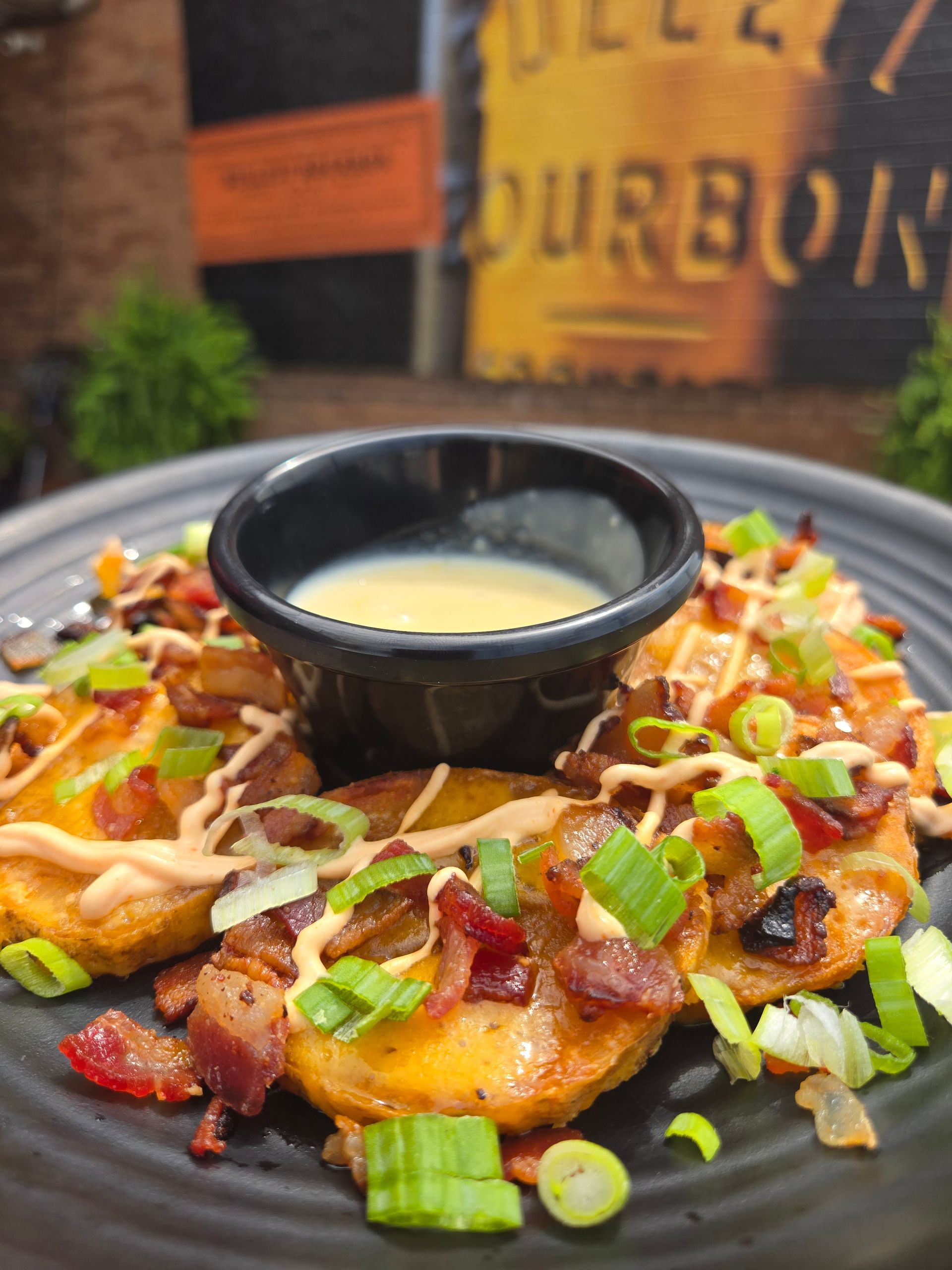 Loaded nachos with bacon, green onions, drizzled sauce, and a central cup of queso dip.