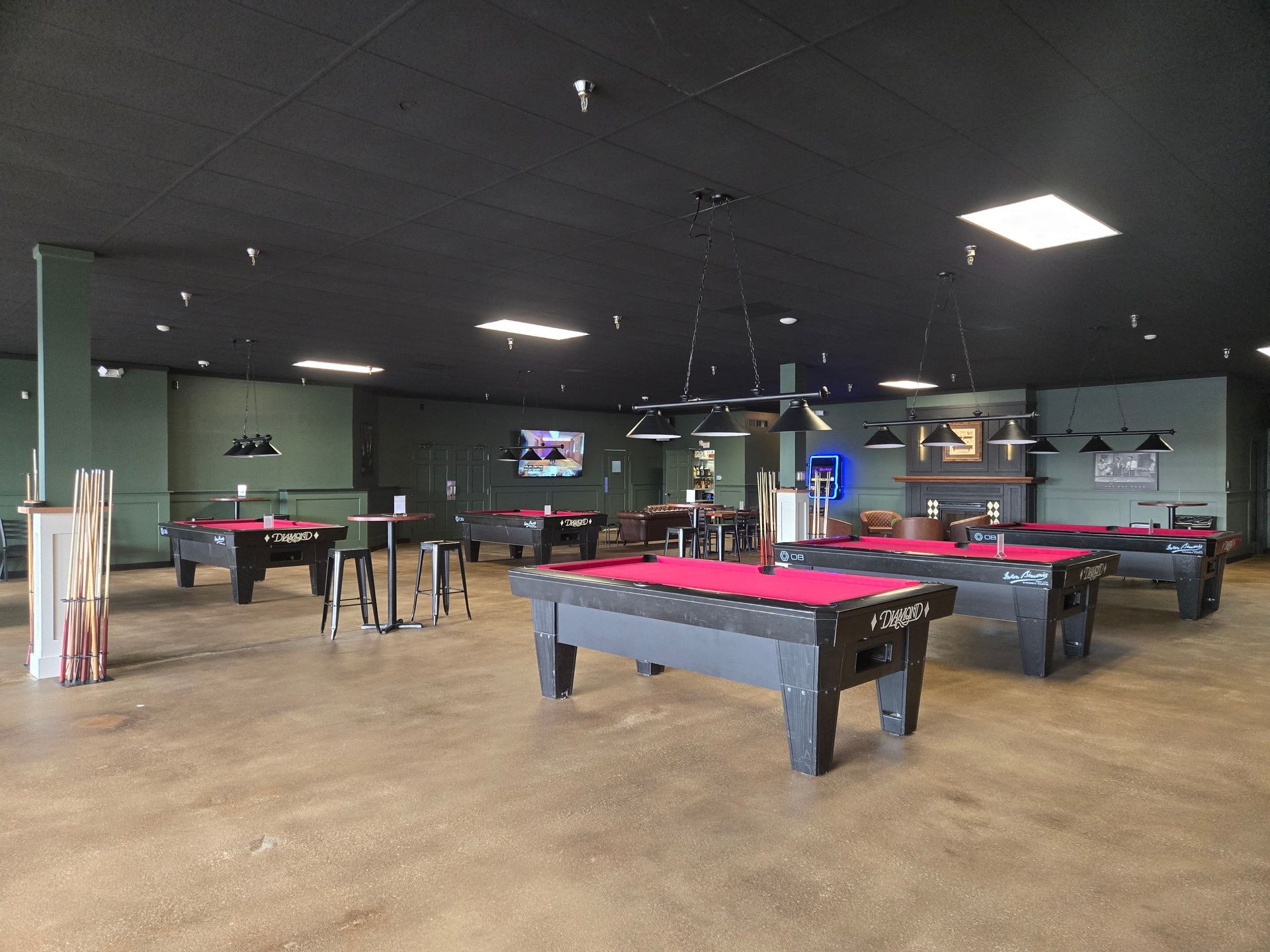 A spacious pool hall with several red-felt billiard tables under hanging lights.