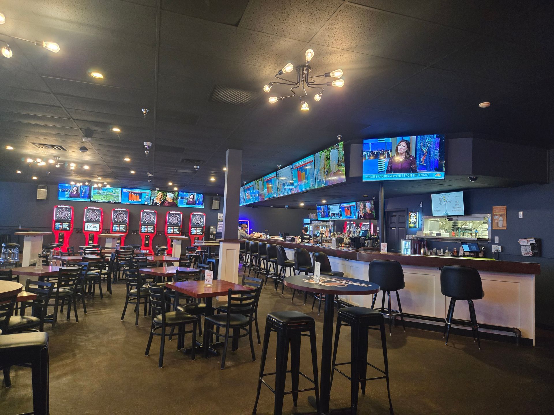 Spacious sports bar with TVs, high tables, stools, and red-lit gaming machines.