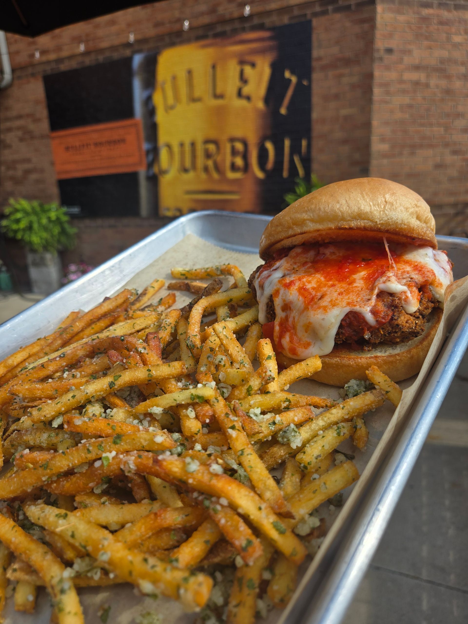 Fries seasoned with herbs beside a cheeseburger on a tray in a restaurant setting