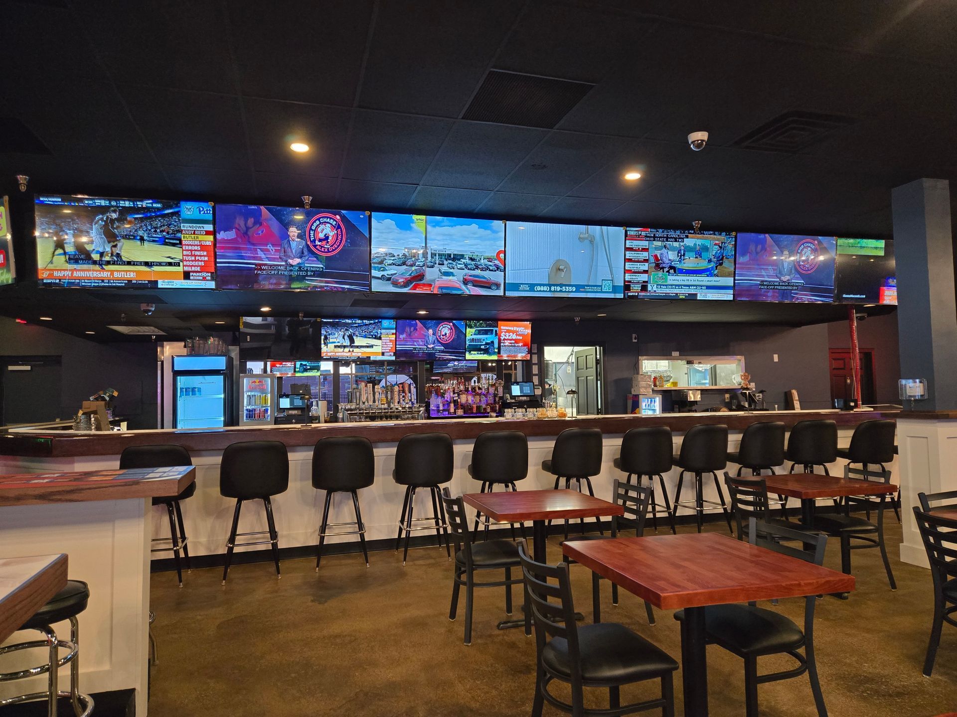 Sports bar interior with TVs above a long counter and tables with chairs in the foreground