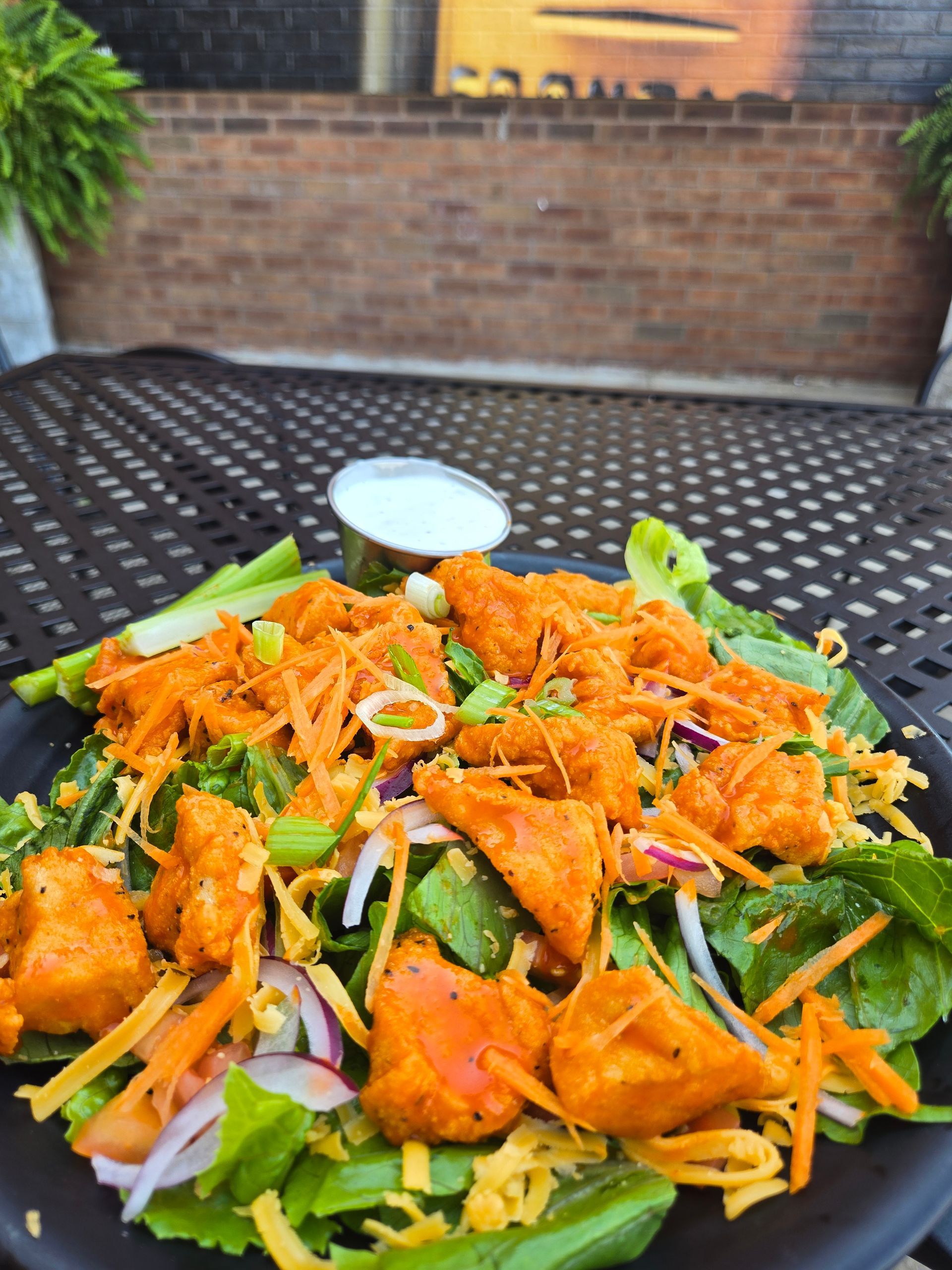 Colorful salad with shredded carrots, lettuce, onions, and crispy toppings on a patterned outdoor table