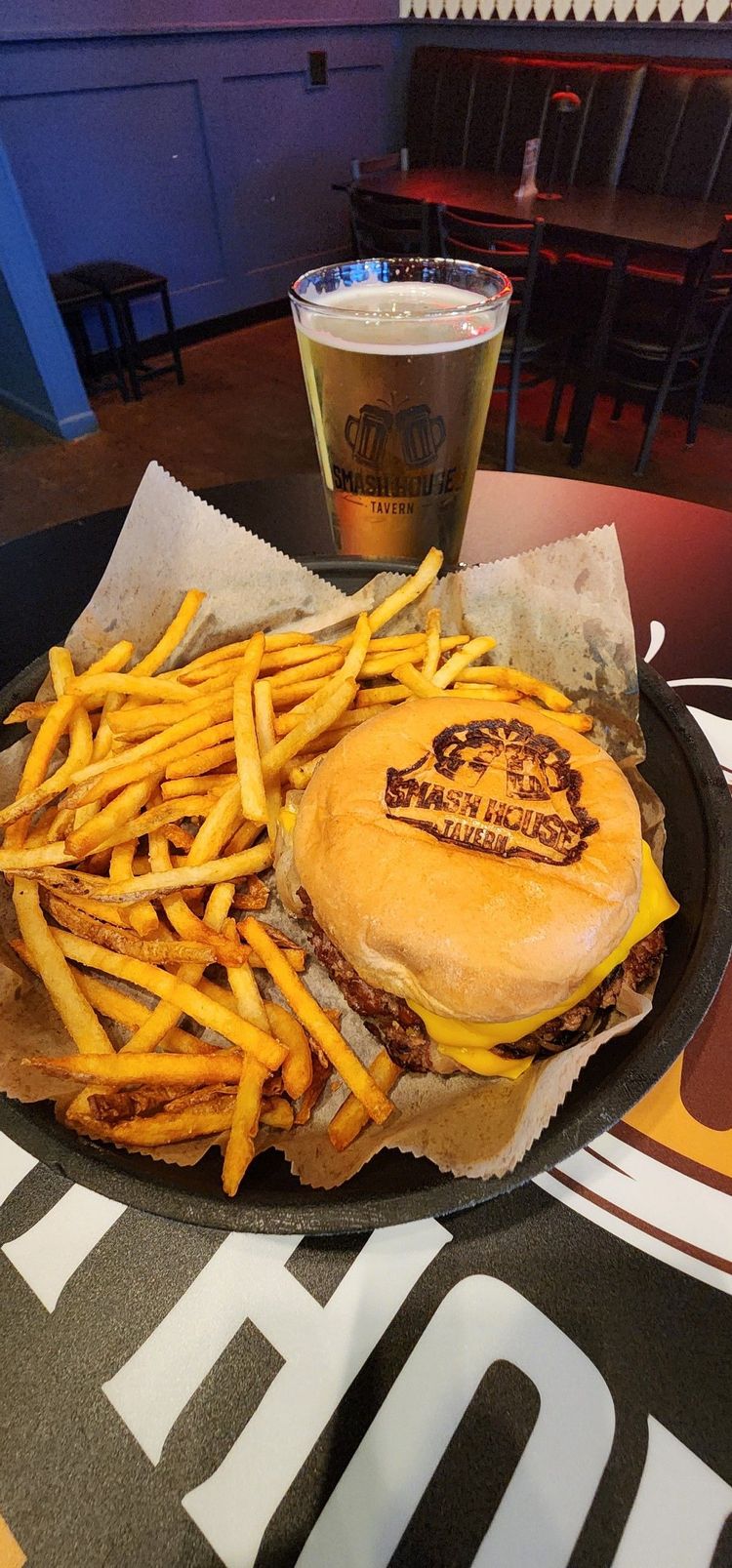 Burger and fries on a plate with a beer in a dimly lit restaurant booth