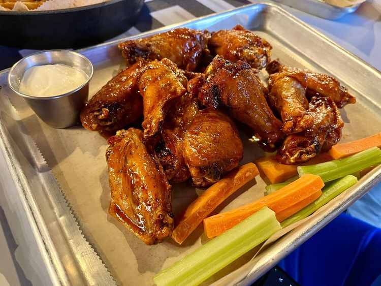 Plate of saucy chicken wings with celery, carrot sticks, and dipping sauce